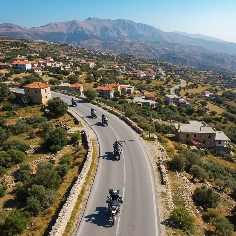 Motorcyclists riding through a traditional Greek village on a curvy road, with charming stone houses and scenic views.